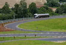 SC atinge 90% das rodovias estaduais recuperadas Caminhão tanque branco trafega em curva de rodovia estadual de Santa Catarina com asfalto novo, sinalização vertical revitalizada e defensas metálicas, ilustrando as melhorias do programa Estrada Boa na infraestrutura viária.