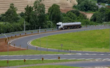 SC atinge 90% das rodovias estaduais recuperadas Caminhão tanque branco trafega em curva de rodovia estadual de Santa Catarina com asfalto novo, sinalização vertical revitalizada e defensas metálicas, ilustrando as melhorias do programa Estrada Boa na infraestrutura viária.