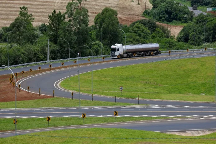 SC atinge 90% das rodovias estaduais recuperadas Caminhão tanque branco trafega em curva de rodovia estadual de Santa Catarina com asfalto novo, sinalização vertical revitalizada e defensas metálicas, ilustrando as melhorias do programa Estrada Boa na infraestrutura viária.