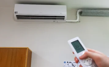 SC é o primeiro estado com 100% das salas climatizadas Aparelho de ar-condicionado split branco instalado em parede de sala de aula da rede estadual de Santa Catarina, com mão segurando controle remoto em primeiro plano, simbolizando a climatização total das escolas pelo programa Escola Boa.