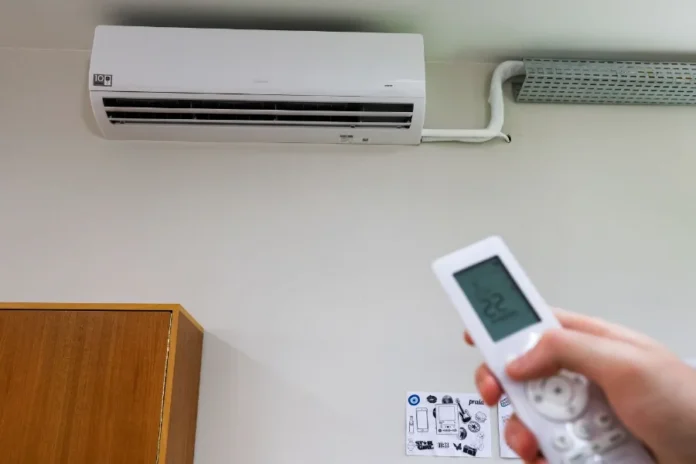 SC é o primeiro estado com 100% das salas climatizadas Aparelho de ar-condicionado split branco instalado em parede de sala de aula da rede estadual de Santa Catarina, com mão segurando controle remoto em primeiro plano, simbolizando a climatização total das escolas pelo programa Escola Boa.