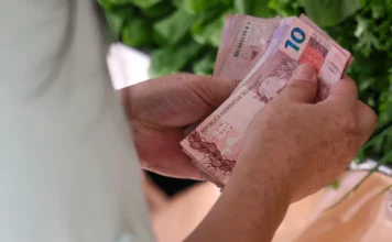 SC tem menor índice de Bolsa Família entre estados Pessoa conta cédulas de dinheiro em Santa Catarina, em imagem relacionada ao Bolsa Família e programas sociais