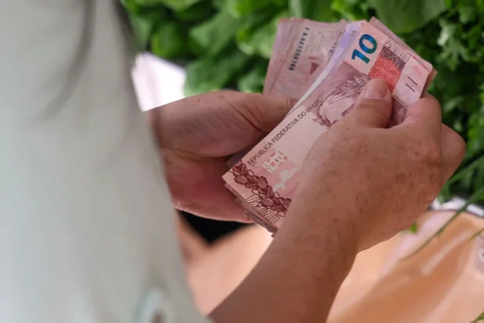 SC tem menor índice de Bolsa Família entre estados Pessoa conta cédulas de dinheiro em Santa Catarina, em imagem relacionada ao Bolsa Família e programas sociais