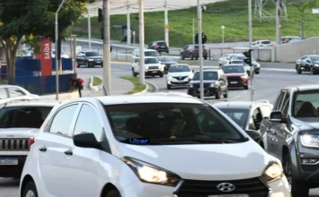 Santa Catarina propõe isenção de IPVA para motoristas de app Carro branco em trânsito urbano com letreiro de LED azul escrito Uber no para-brisa, representando motoristas de aplicativos que podem receber isenção de IPVA em Santa Catarina através de projeto na Alesc.