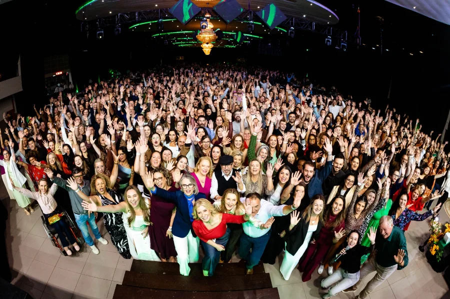 Grande grupo de colaboradores, professores e lideranças da Unesc reunidos na AM Master Hall em celebração ao Dia do Trabalhador, destacando a integração e valorização da comunidade acadêmica.