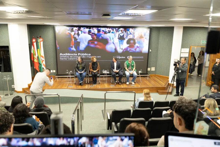 Audiência pública na Alesc debate direitos da população migrante em Santa Catarina, com representantes no plenário e participantes acompanhando a discussão