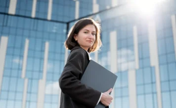 Carreira em T ganha força com avanço da tecnologia Profissional com notebook em frente a prédio corporativo representa carreira em T, tecnologia e perfil multidisciplinar no mercado de trabalho.