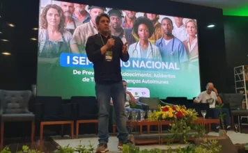 Conferência vai debater futuro da saúde em Criciúma Palestrante durante conferência de saúde em Criciúma com painel sobre o SUS e políticas públicas de saúde ao fundo.