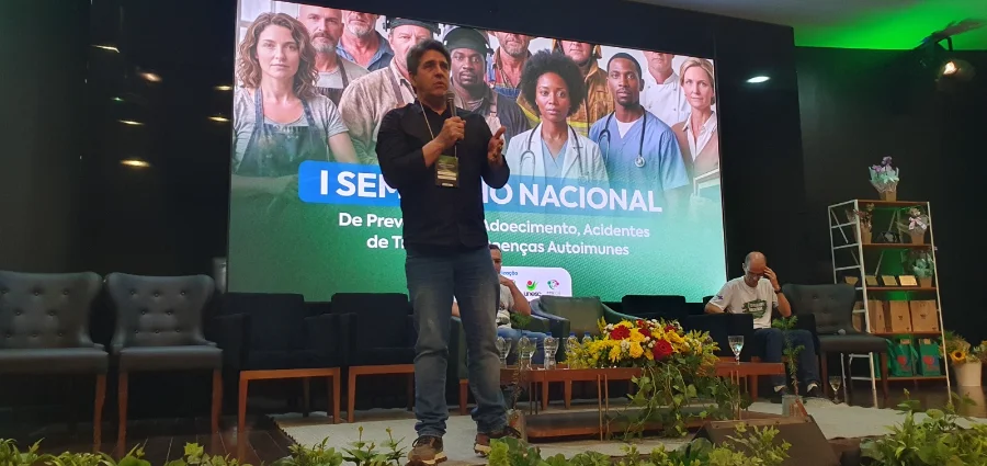 Palestrante durante conferência de saúde em Criciúma com painel sobre o SUS e políticas públicas de saúde ao fundo.
