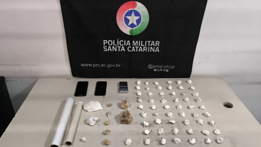 Drogas apreendidas pela Polícia Militar em Sombrio, com porções de cocaína e crack, balança de precisão e celulares sobre mesa.
