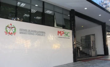 MPSC aciona Sombrio por descumprir decisão na saúde mental Fachada da sede do Ministério Público de Santa Catarina (MPSC), com parede branca revestida de azulejos onde se destacam o brasão do Estado de Santa Catarina e a logomarca oficial do MPSC em vermelho e verde, ao lado da rampa e escadaria de acesso ao prédio.