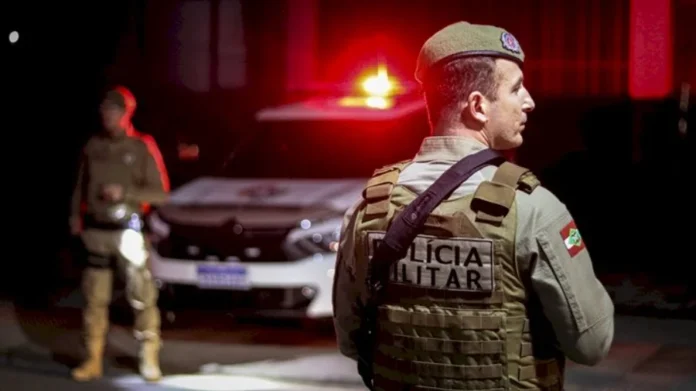 PMSC cumpre 1.445 mandados em operação no estado Policial militar da PMSC em operação noturna com viatura ao fundo durante cumprimento de mandados em Santa Catarina