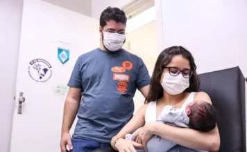 Agosto Dourado reforça apoio à amamentação em 2026 Mãe amamenta bebê durante atendimento em banco de leite humano, com acompanhante ao lado, em ação do Agosto Dourado.