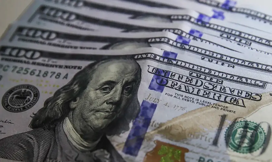 Notas de 100 dólares ilustram queda de 23,1% na ajuda internacional dos países ricos em 2025.
