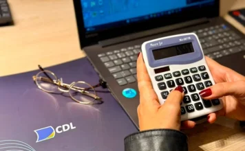 CDL Araranguá promove oficina gratuita de precificação Mãos utilizam calculadora sobre mesa com notebook e pasta da CDL, ilustrando oficina gratuita de precificação para empreendedores em Araranguá.