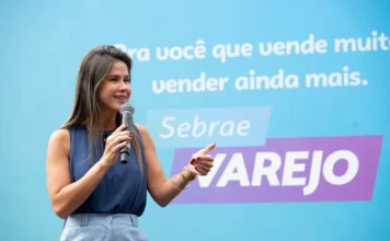 CDL Criciúma realiza workshop sobre vendas em alta performance Fabrícia Borba, especialista em marketing e vendas e consultora do Sebrae, palestranda com um microfone na mão em um evento de capacitação para o varejo da CDL Criciúma. O fundo é azul com texto de apoio.