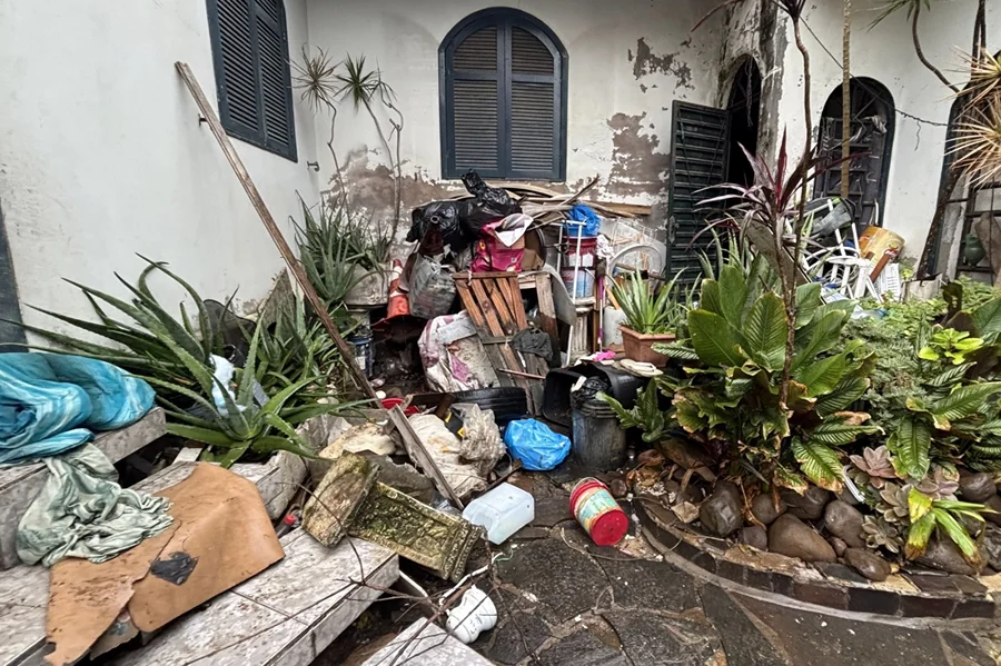 Área externa de residência no Centro de Criciúma com grande acúmulo de resíduos, móveis e materiais inservíveis durante intervenção da Prefeitura.