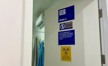 Raio-x em Siderópolis atinge 5,6 mil exames em um ano Porta branca da sala de raio-x na Policlínica São Lucas em Siderópolis, com placas de sinalização azul e amarela indicando acesso restrito e avisos de segurança sobre radiação e gravidez.