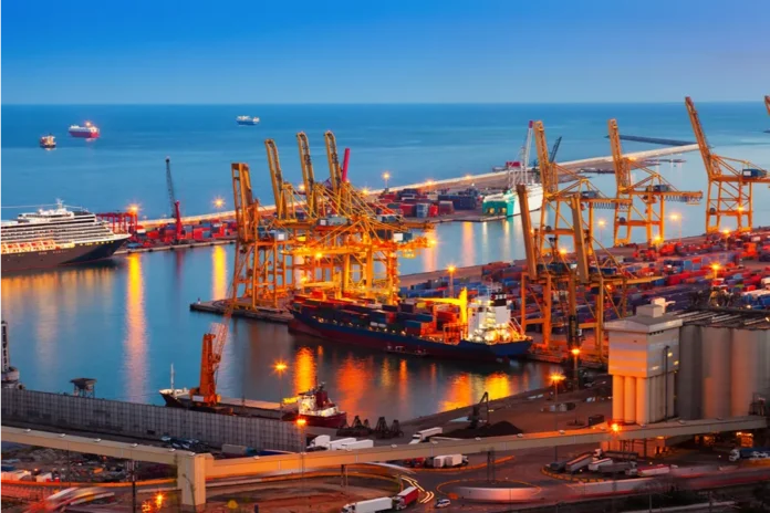 FIESC lidera missão empresarial à Expo Paraguay-Brasil 2026 Vista aérea de um porto comercial movimentado e iluminado ao anoitecer, destacando navios cargueiros, grandes guindastes amarelos e pilhas de contêineres. A infraestrutura logística ilustra o setor de comércio exterior, a exportação e a internacionalização da indústria catarinense, temas centrais da missão empresarial da FIESC na Expo Paraguay-Brasil.