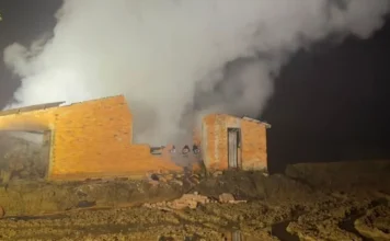 Incêndio destrói dois depósitos de madeira em Jacinto Machado Edificação destruída por incêndio em Jacinto Machado, com intensa fumaça branca saindo das ruínas de tijolos durante a noite. O terreno agrícola e enlameado é iluminado pelos refletores do Corpo de Bombeiros durante o trabalho de rescaldo.