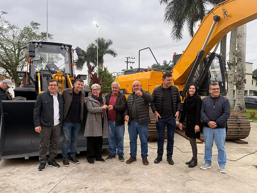 Autoridades municipais posam ao lado de escavadeira e máquinas entregues pela Prefeitura de Jacinto Machado para reforçar Obras e Agricultura.