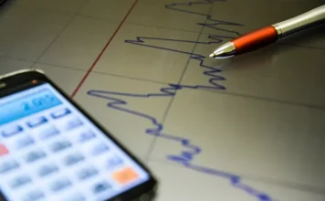 Mercado reduz projeção do PIB do Brasil para 1,95% em 2026 Gráfico de mercado financeiro com celular e caneta ilustra projeções do Boletim Focus para PIB, inflação, Selic e dólar em 2026.