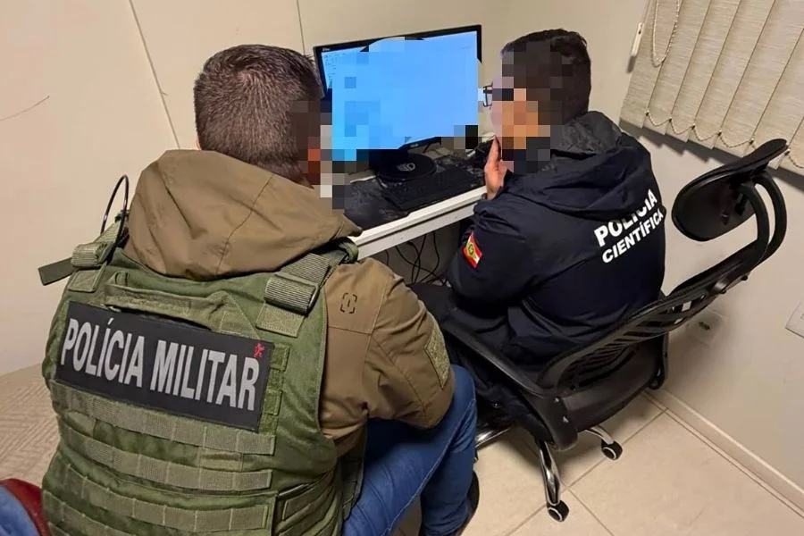Agentes da Polícia Militar e da Polícia Científica analisam computador durante a Operação Digital Footprint, em Araranguá, contra abuso sexual infantojuvenil.