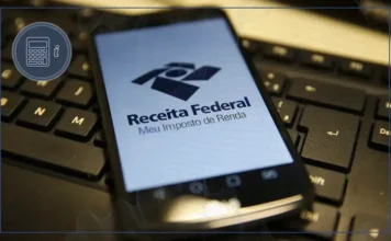 Receita abre consulta ao último lote do IRPF de 2026 Celular exibe a página Meu Imposto de Renda da Receita Federal sobre teclado de computador, em referência à consulta da restituição do IRPF 2026.