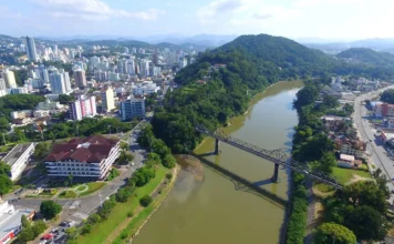 SESI lança programa para atrair verbas a projetos em SC Vista aérea de Blumenau (SC), mostrando o centro urbano, o Rio Itajaí-Açu e a histórica Ponte de Ferro (Ponte Aldo Pereira de Andrade) em direção ao morro arborizado.