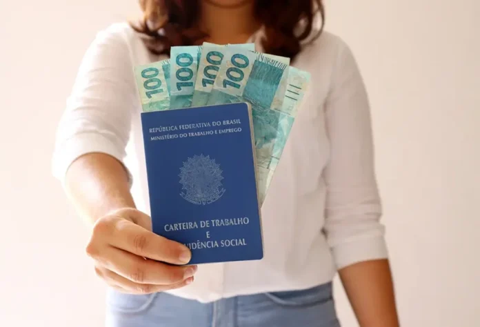 Serviços lideram geração de empregos em Santa Catarina Mulher segura carteira de trabalho e notas de real, representando a geração de empregos formais no setor de serviços em Santa Catarina.