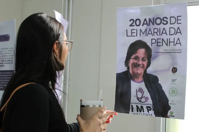 Unesc promove exposição pelos 20 anos da Lei Maria da Penha Mulher observa painel da exposição sobre os 20 anos da Lei Maria da Penha na Unesc.