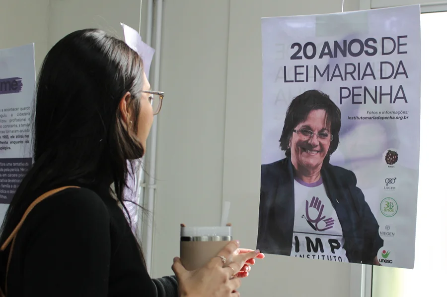 Unesc promove exposição pelos 20 anos da Lei Maria da Penha Mulher observa painel da exposição sobre os 20 anos da Lei Maria da Penha na Unesc.