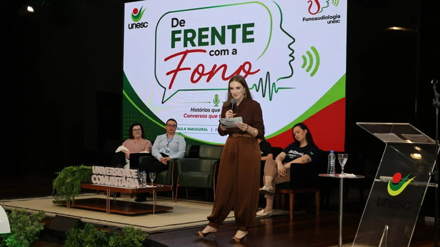 Unesc realiza aula inaugural de Fonoaudiologia em Criciúma Aula inaugural do curso de Fonoaudiologia da Unesc em Criciúma, com participante falando no palco durante o evento “De Frente com a Fono”.