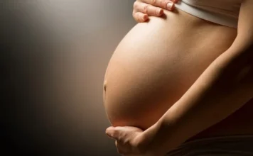 Urussanga retoma curso gratuito para gestantes na quarta Close-up em perfil da barriga de uma mulher grávida com as mãos delicadamente segurando o ventre. Foto ilustrativa para artigo sobre o curso gratuito de gestantes "Colo que Aquece" em Urussanga, abordando temas como pré-natal e maternidade.