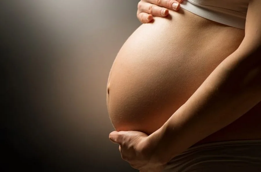 Close-up em perfil da barriga de uma mulher grávida com as mãos delicadamente segurando o ventre. Foto ilustrativa para artigo sobre o curso gratuito de gestantes 