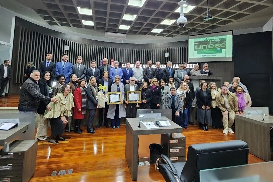 Grupo de autoridades, servidores e representantes da Unesc reunido no plenário da Câmara de Vereadores de Araranguá após entrega de homenagem.