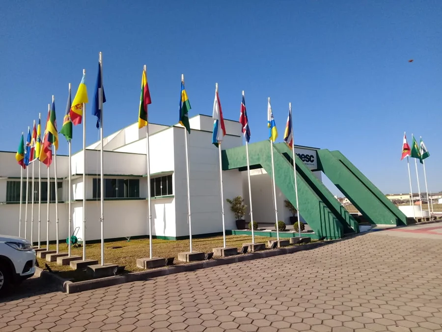 Fachada da sede da AMESC, em Araranguá, com bandeiras dos municípios e estrutura verde na entrada.