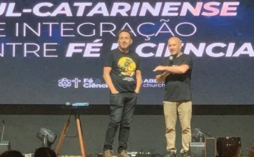 Criciúma terá simpósio gratuito para debater fé e ciência Dois homens no palco, um deles com microfone, diante de painel do Simpósio Sul Catarinense de Integração entre Fé e Ciência, em Criciúma.