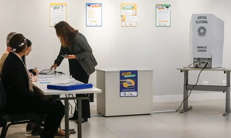 Eleitora entrega celular antes de acessar a cabine de votação durante as eleições de 2026.