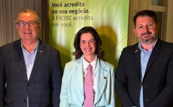 Ex-presidente da ACIVA assume liderança regional na FACISC Três representantes do setor empresarial posam diante de um painel da FACISC.