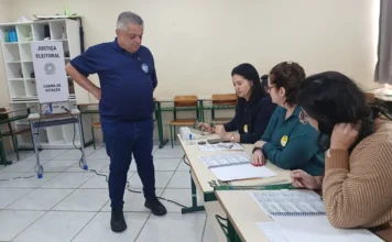 João Rodrigues vota em Chapecó e aposta no segundo turno João Rodrigues diante da mesa de mesárias na Escola Professora Zélia Scharf, em Chapecó, durante as eleições 2026.
