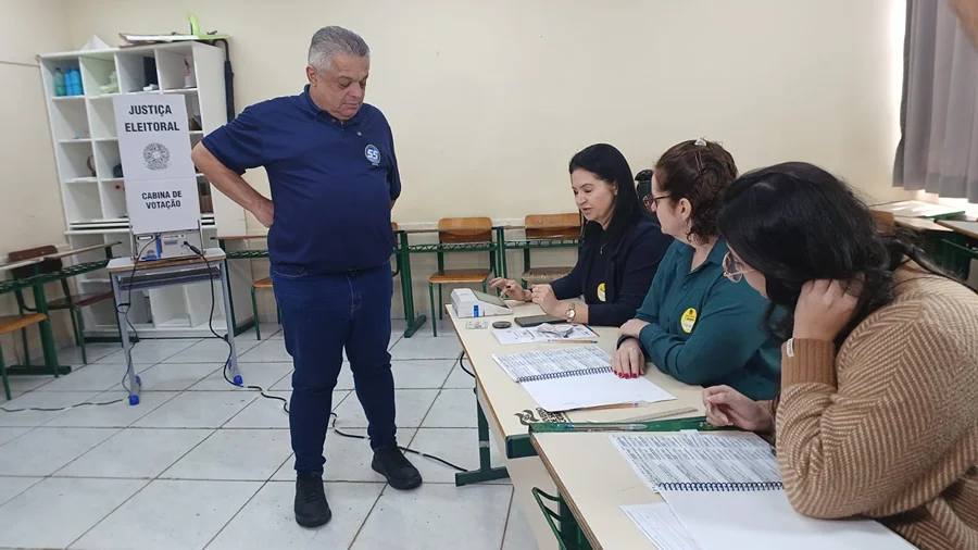 João Rodrigues diante da mesa de mesárias na Escola Professora Zélia Scharf, em Chapecó, durante as eleições 2026.