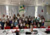 Estudantes fantasiados exibem kits educativos ao lado de adultos em sala de aula de Maracajá durante comemoração do Dia das Crianças.