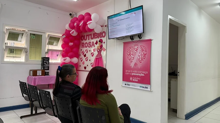 Outubro Rosa 2025 Morro da Fumaca 1 Mulheres sentadas em sala de espera de unidade de saúde de Morro da Fumaça, decorada com balões e cartazes do Outubro Rosa.