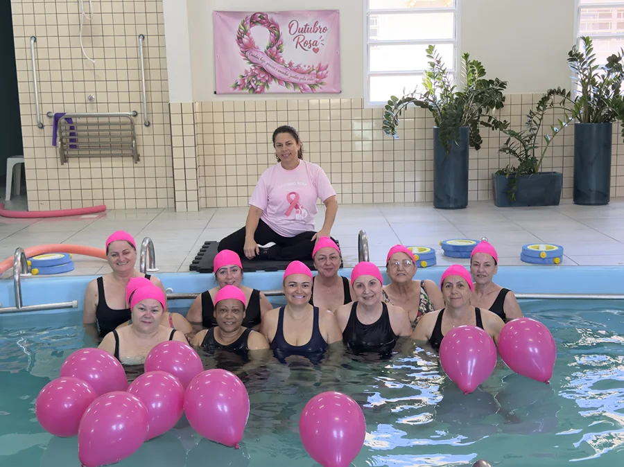Alunas de hidroginástica usam toucas rosas em piscina com balões da mesma cor durante ação do Outubro Rosa em Morro da Fumaça.