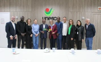 Unesc recebe representante do Togo e debate intercâmbio Representantes da Unesc e do Togo reunidos em Criciúma, com pequenas bandeiras dos dois países ao centro.