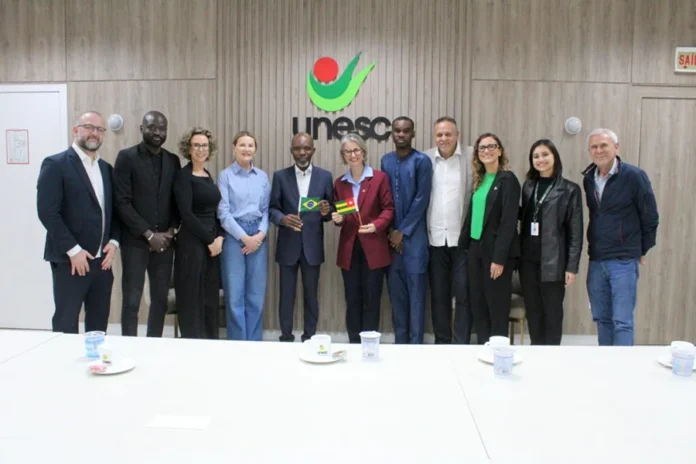 Unesc recebe representante do Togo e debate intercâmbio Representantes da Unesc e do Togo reunidos em Criciúma, com pequenas bandeiras dos dois países ao centro.
